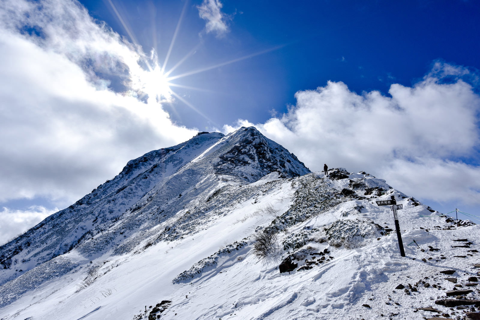 雪山の赤岳山頂付近で太陽光が光芒となって差し込む中を歩く登山者