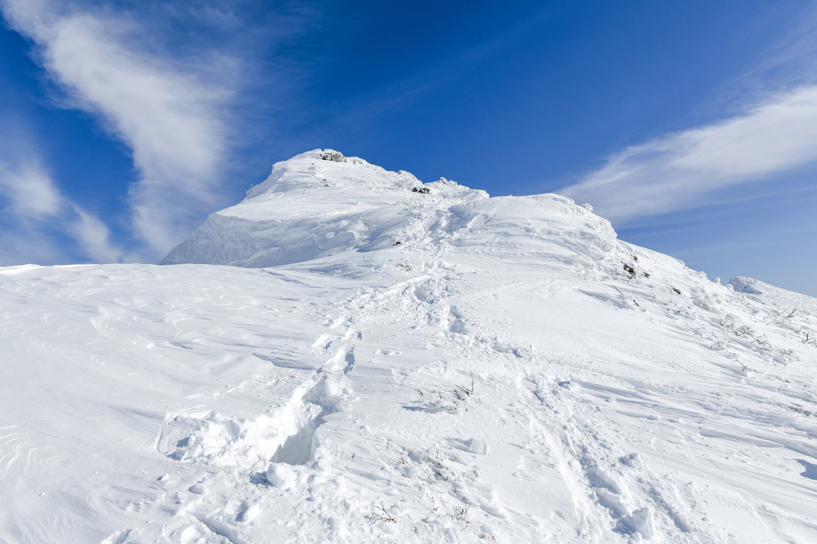 青空の下、雪に覆われた谷川岳オキの耳と登山道の足跡