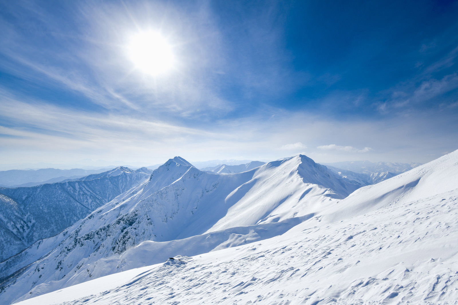 青空と太陽の下に雪化粧した谷川岳の山脈が広がる風景