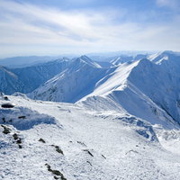 午後の日差しを浴びて陰影が濃くなる雪の谷川岳主脈の写真