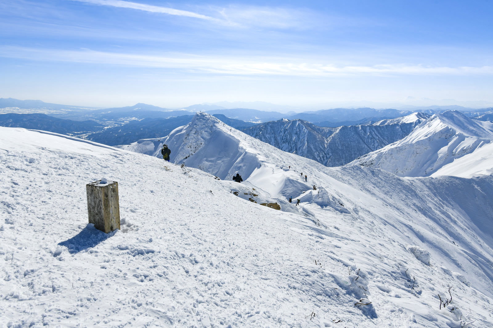 雪に埋もれた山頂碑の向こうに広がる雪化粧した谷川岳トマの耳方面の稜線