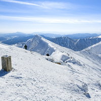 雪に埋まった山頂碑から見る谷川岳トマの耳方面の写真