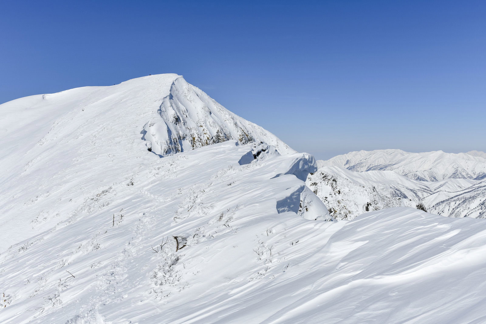 青空の下、真っ白な雪で覆われた谷川岳の山頂と稜線