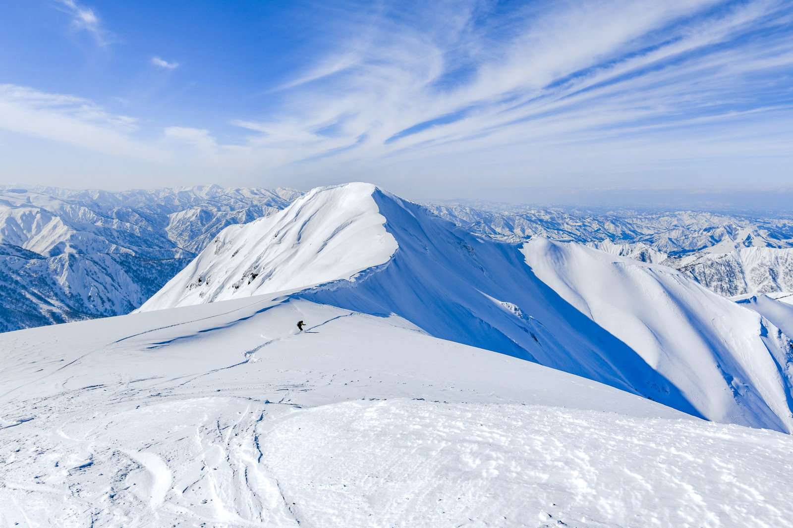 青空の下、雪に覆われた茂倉岳の山頂付近に発達した雪庇が見える雪山風景