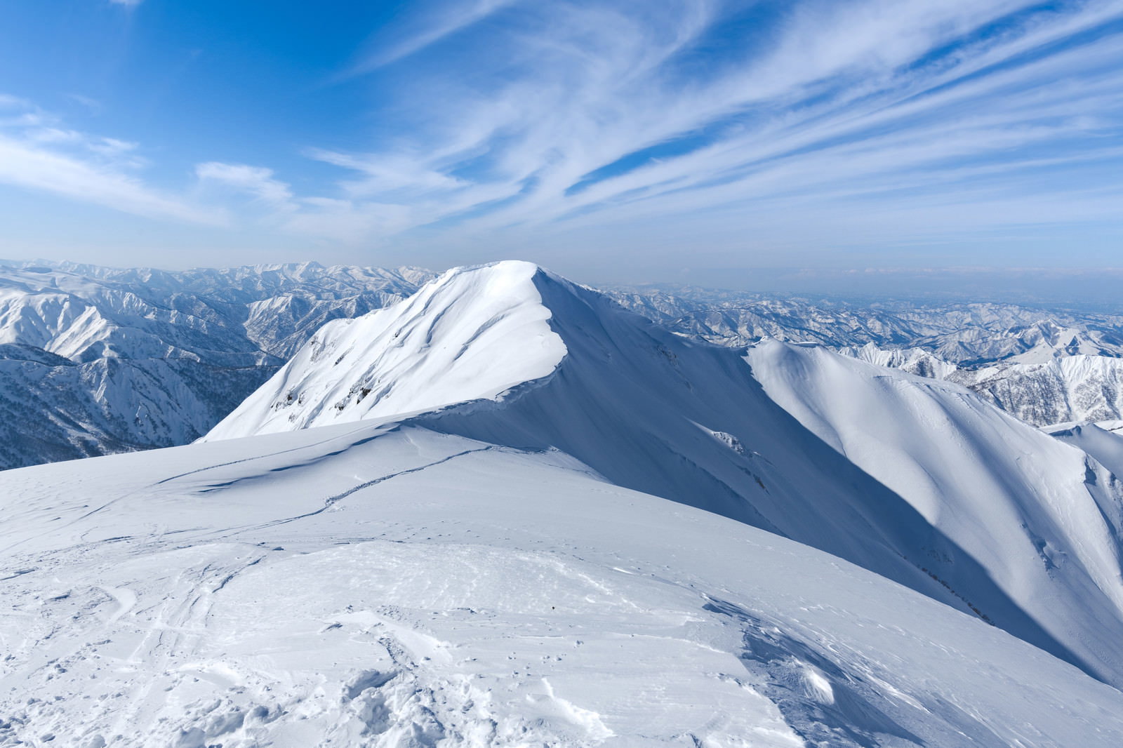 青空の下、雪化粧した茂倉岳の斜面を滑走するスノーボーダー