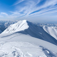 茂倉岳の斜面へとドロップしてゆく青空下のスノーボーダーの写真