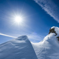 青空に飛行機雲が流れる、雪の谷川岳山肌に照り付ける太陽の写真
