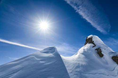 青空に飛行機雲が流れる、雪の谷川岳山肌に照り付ける太陽
