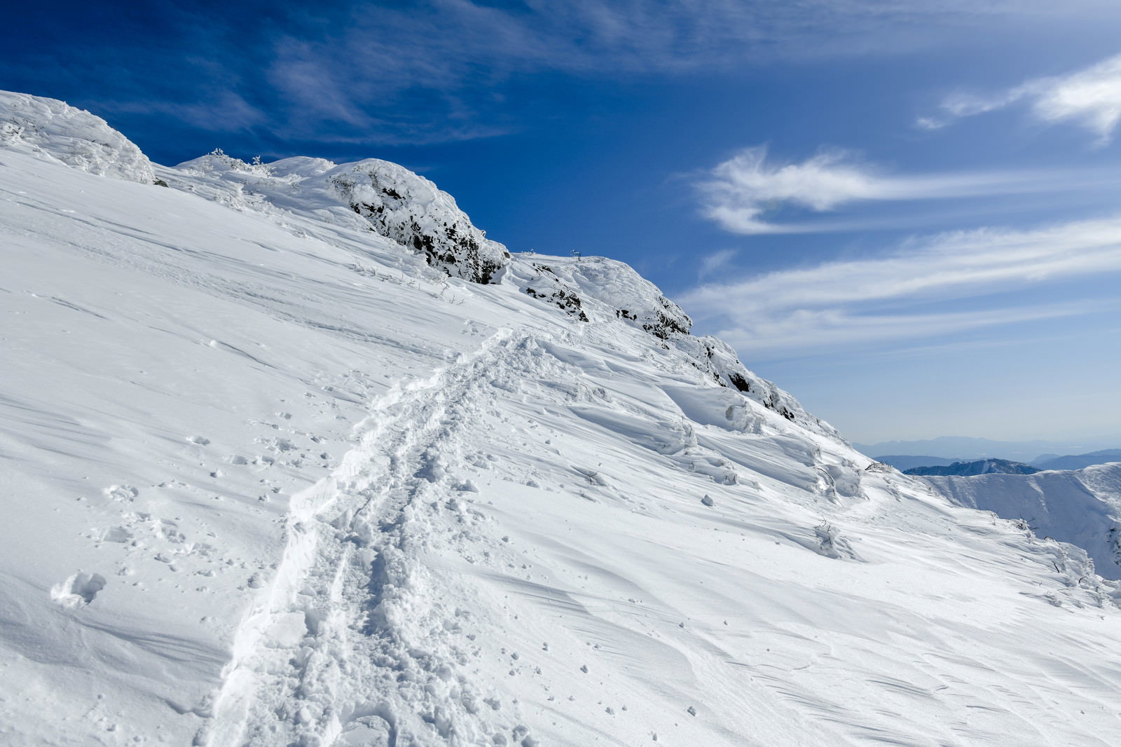 谷川岳の雪景色、白い斜面に続く一筋の足跡と青空