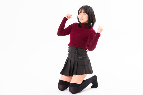 赤いトップスで膝立ちガッツポーズを決める笑顔の女性