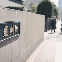 裁判所の銘板の前を行き交う通行人たちと石造りの建物の写真