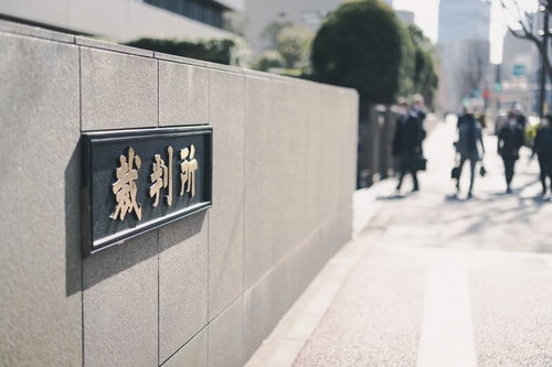 裁判所の銘板の前を行き交う通行人たちと石造りの建物