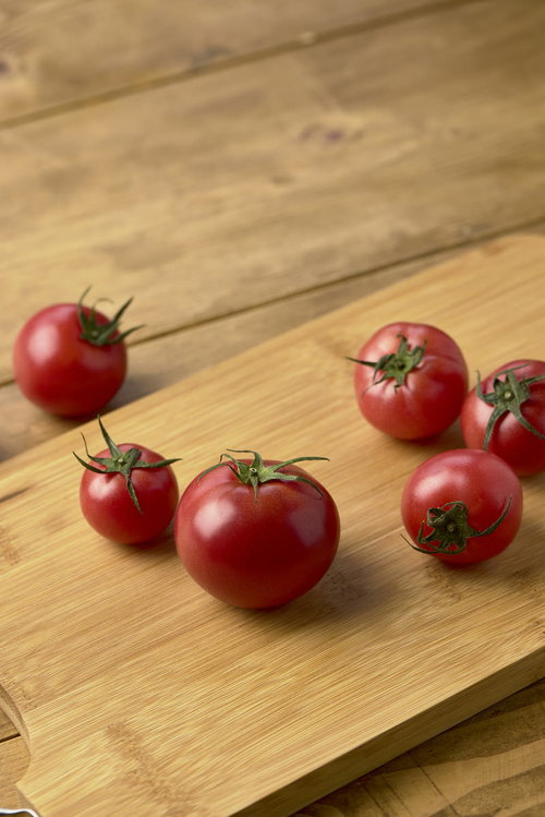 木製カッティングボードに転がったへた付きのミニトマト