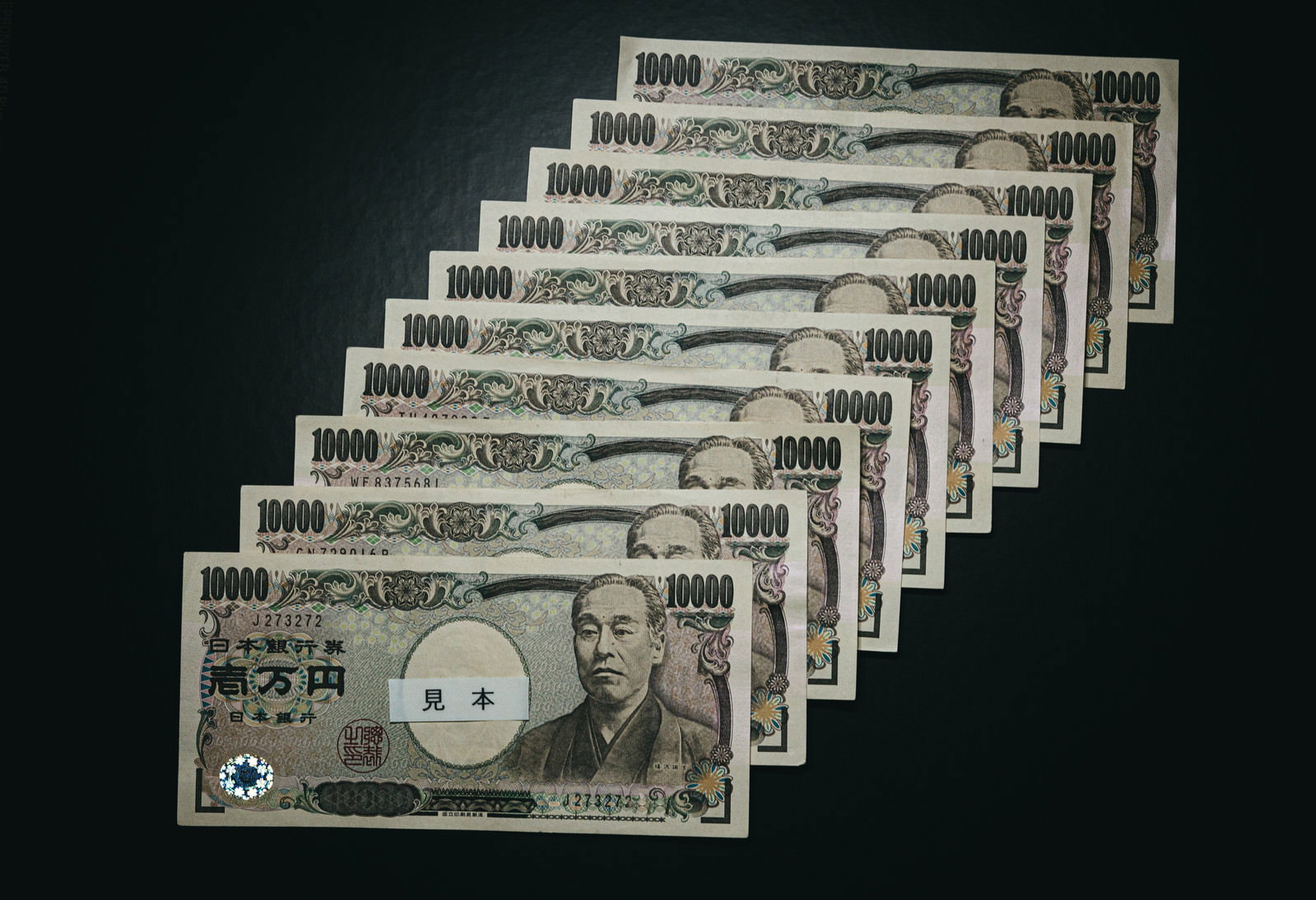 黒い背景に扇状に重ねて並べられた複数の一万円札