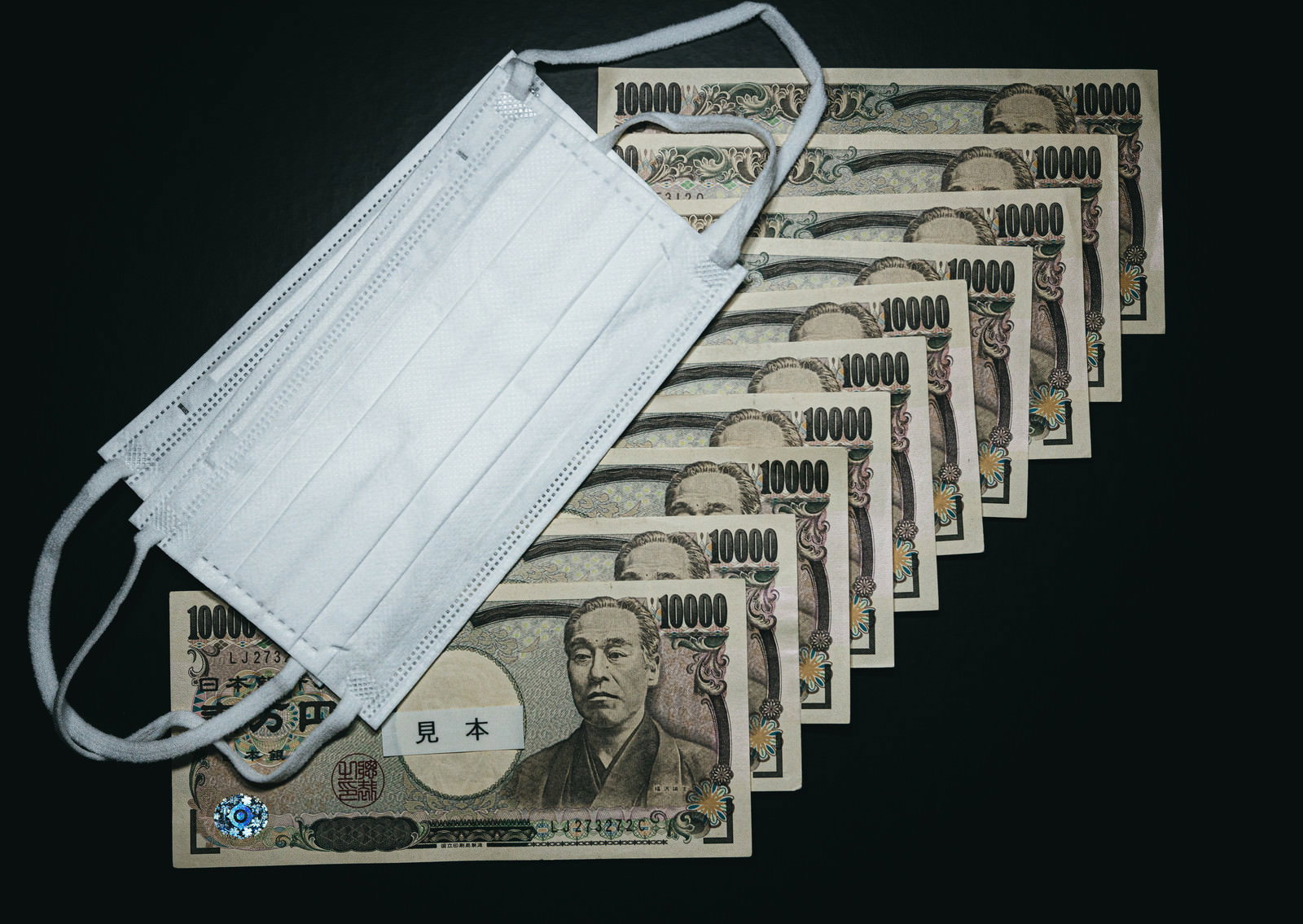 一万円札10枚の上に白いマスク2枚が置かれた給付金のイメージ