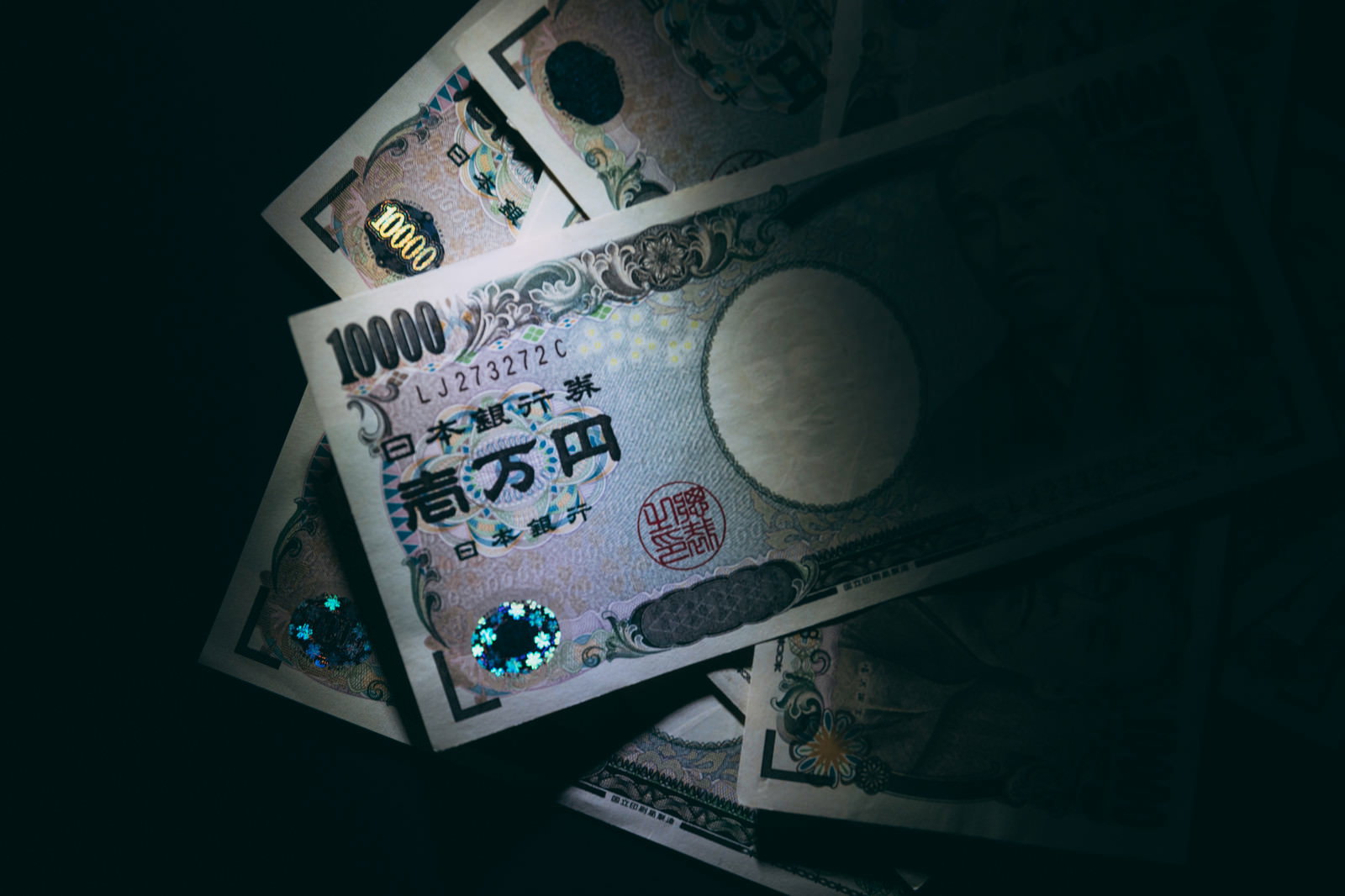 暗い背景に散らばって重なり合う複数の一万円札