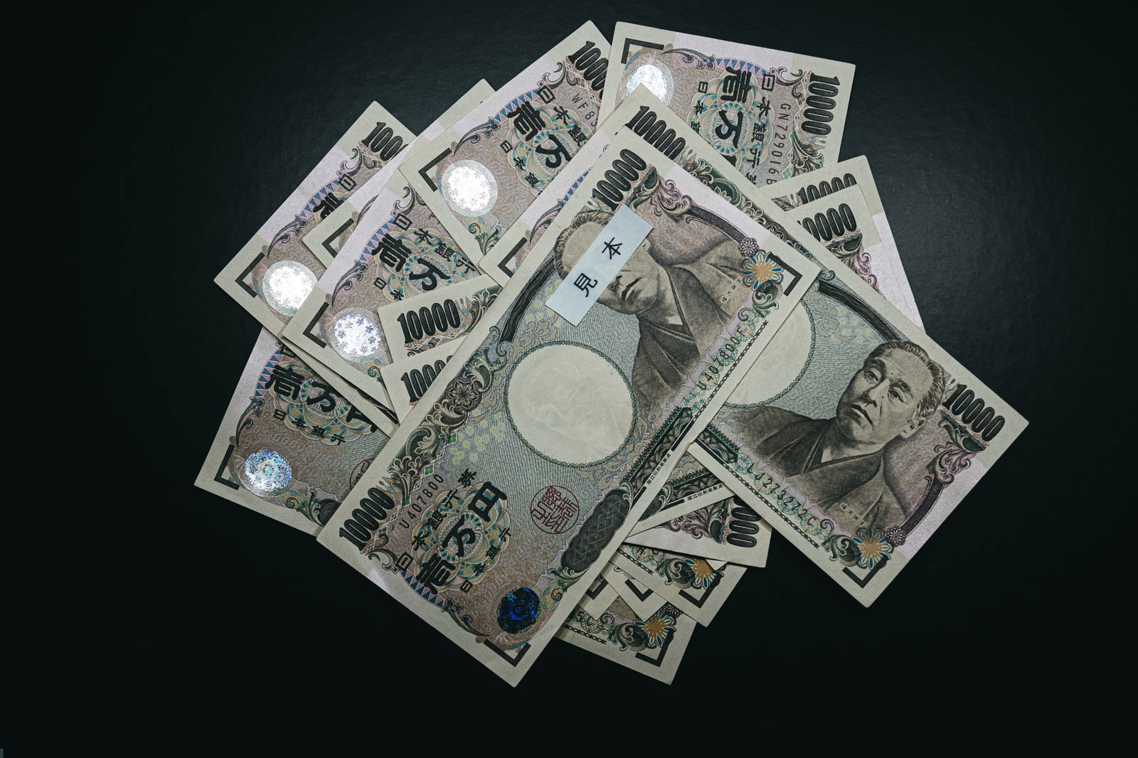 黒い背景に散らばって重なり合う複数枚の一万円札