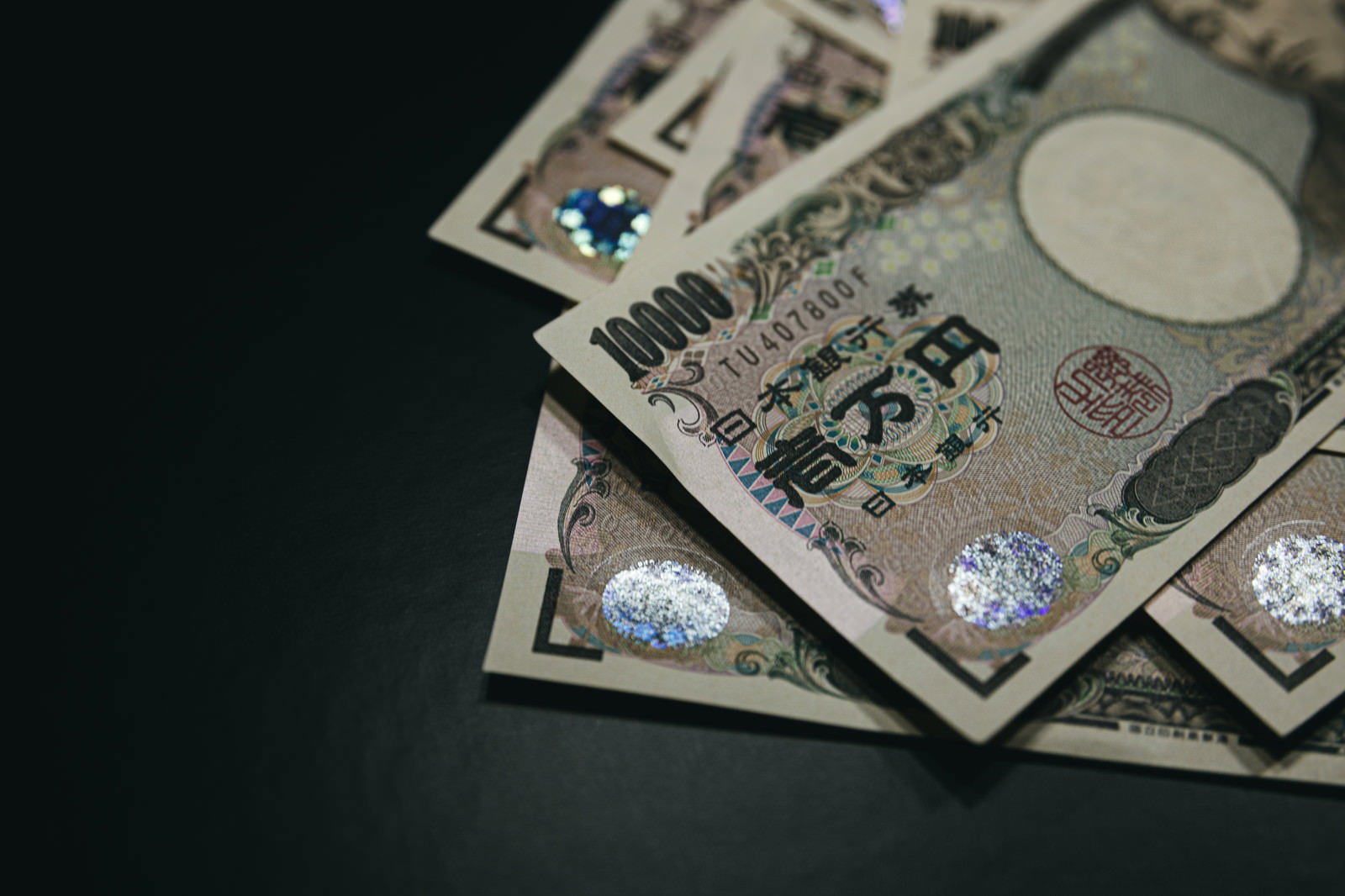 暗い背景に散らばって重なり合う複数の一万円札