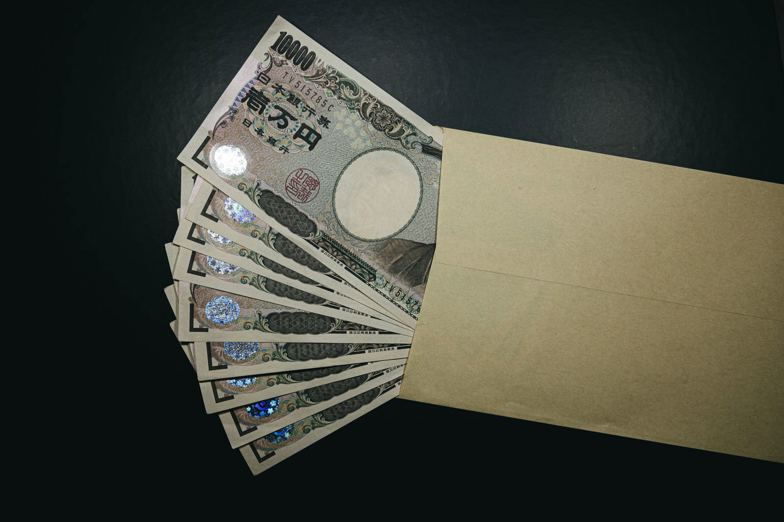 ベージュ色の封筒から扇状に広がった複数の一万円札