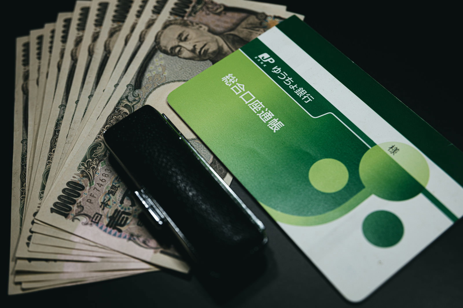緑色の通帳の上に置かれた10万円分の一万円札と銀行印