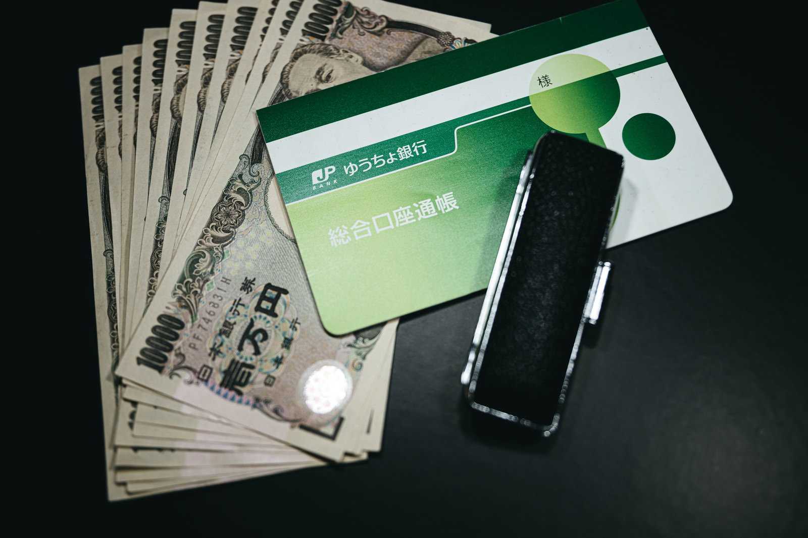 緑色のクレジットカードと一万円札、黒いスマートフォンが並んで置かれている