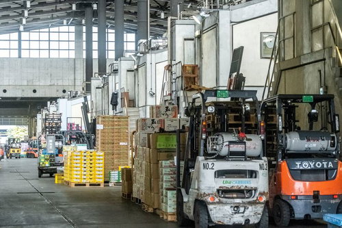 市場の倉庫内で段ボール箱を運ぶオレンジ色のフォークリフト
