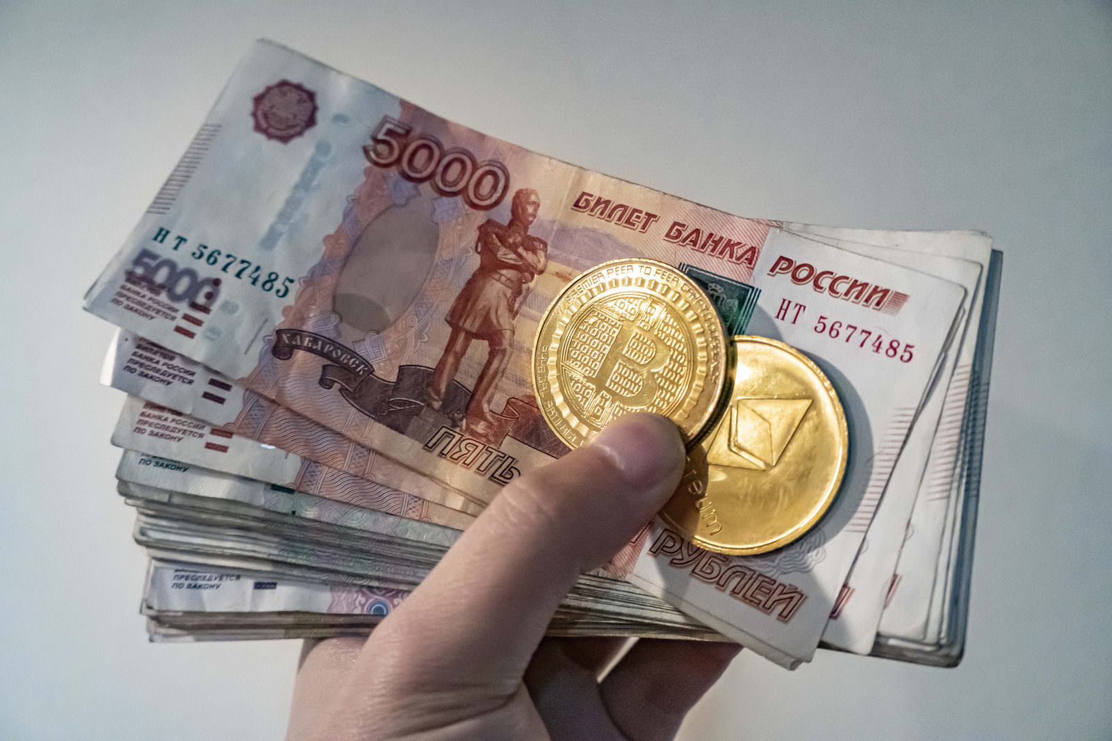 手に持ったロシアルーブル紙幣と金色のビットコイン・イーサリアムコイン