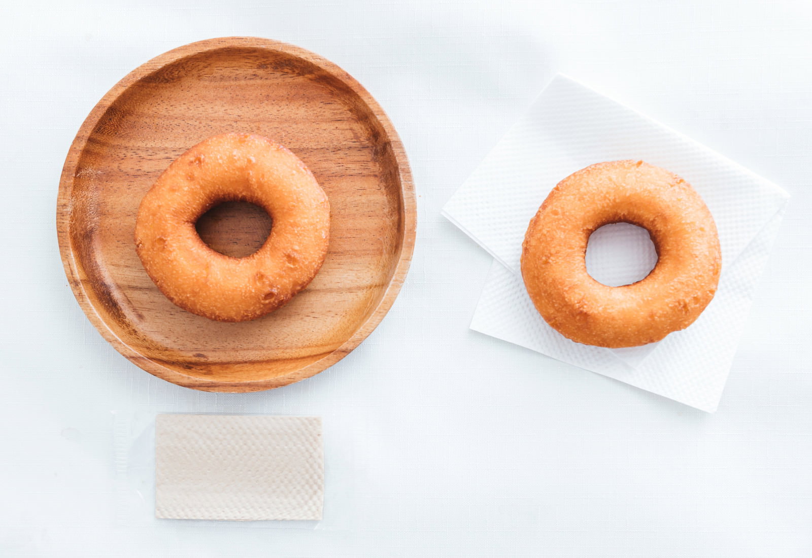 木の丸皿に載ったドーナッツと白い紙袋に入ったドーナッツが並んで置かれている