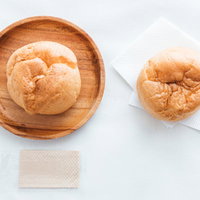 木製のお皿に盛られたシュークリーム2つ、カスタードクリーム入りの写真