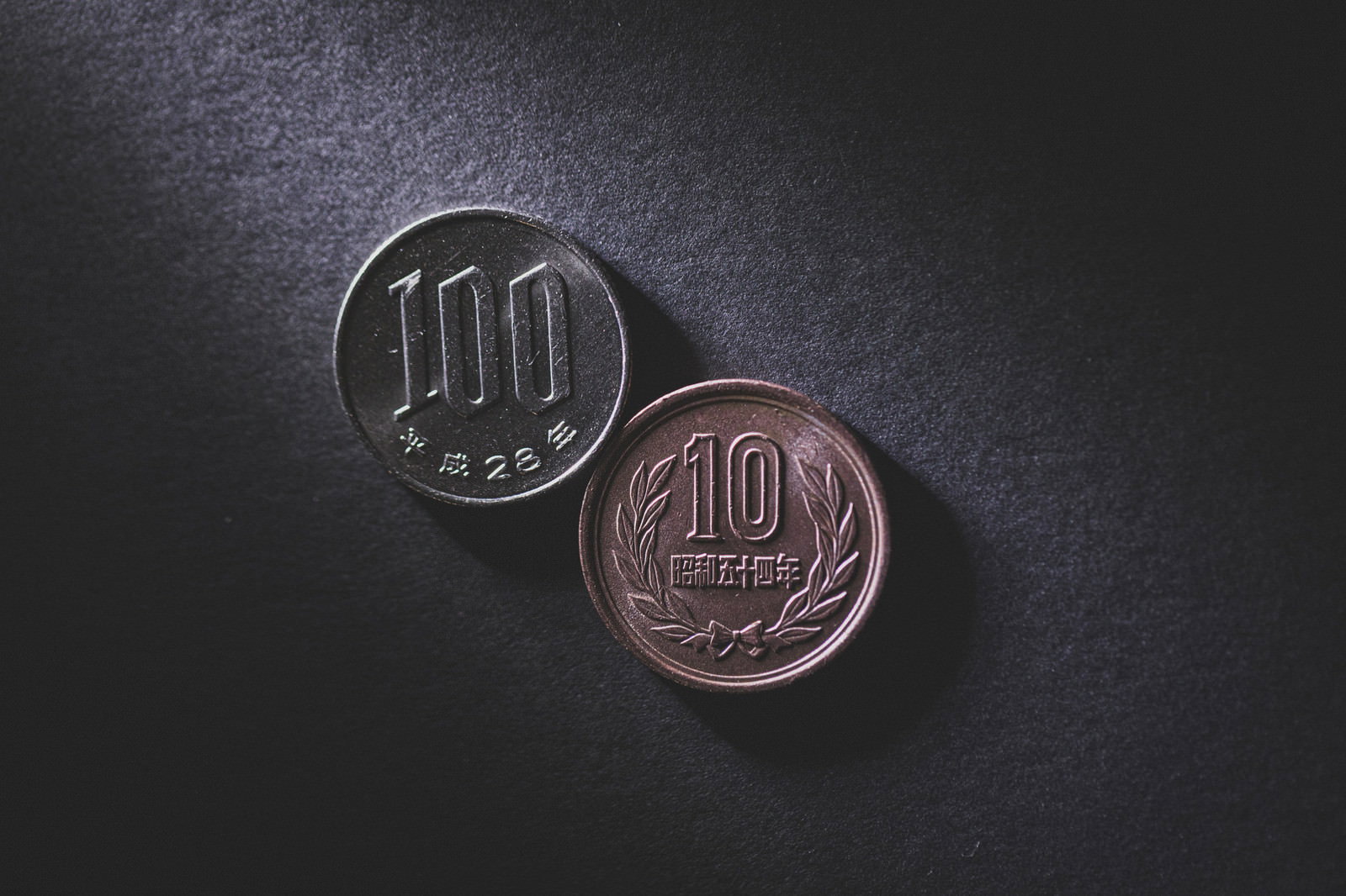 黒い背景に置かれた100円硬貨と10円硬貨