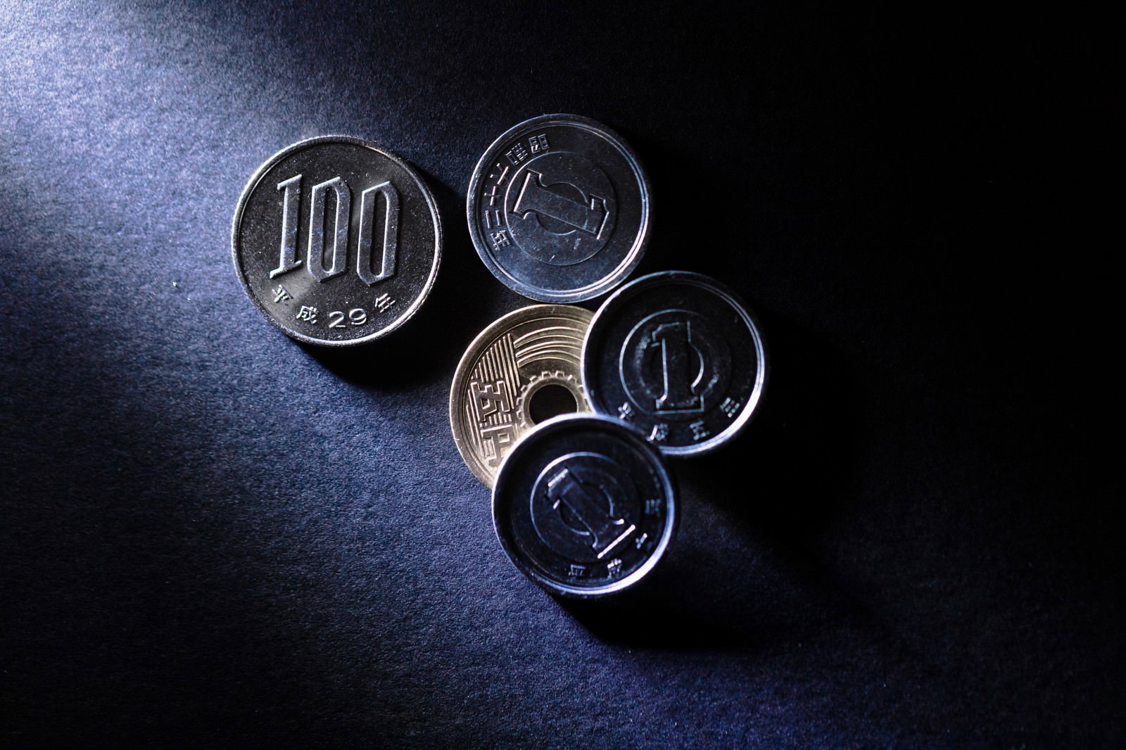 暗い背景に散らばった複数の硬貨が光を反射している様子