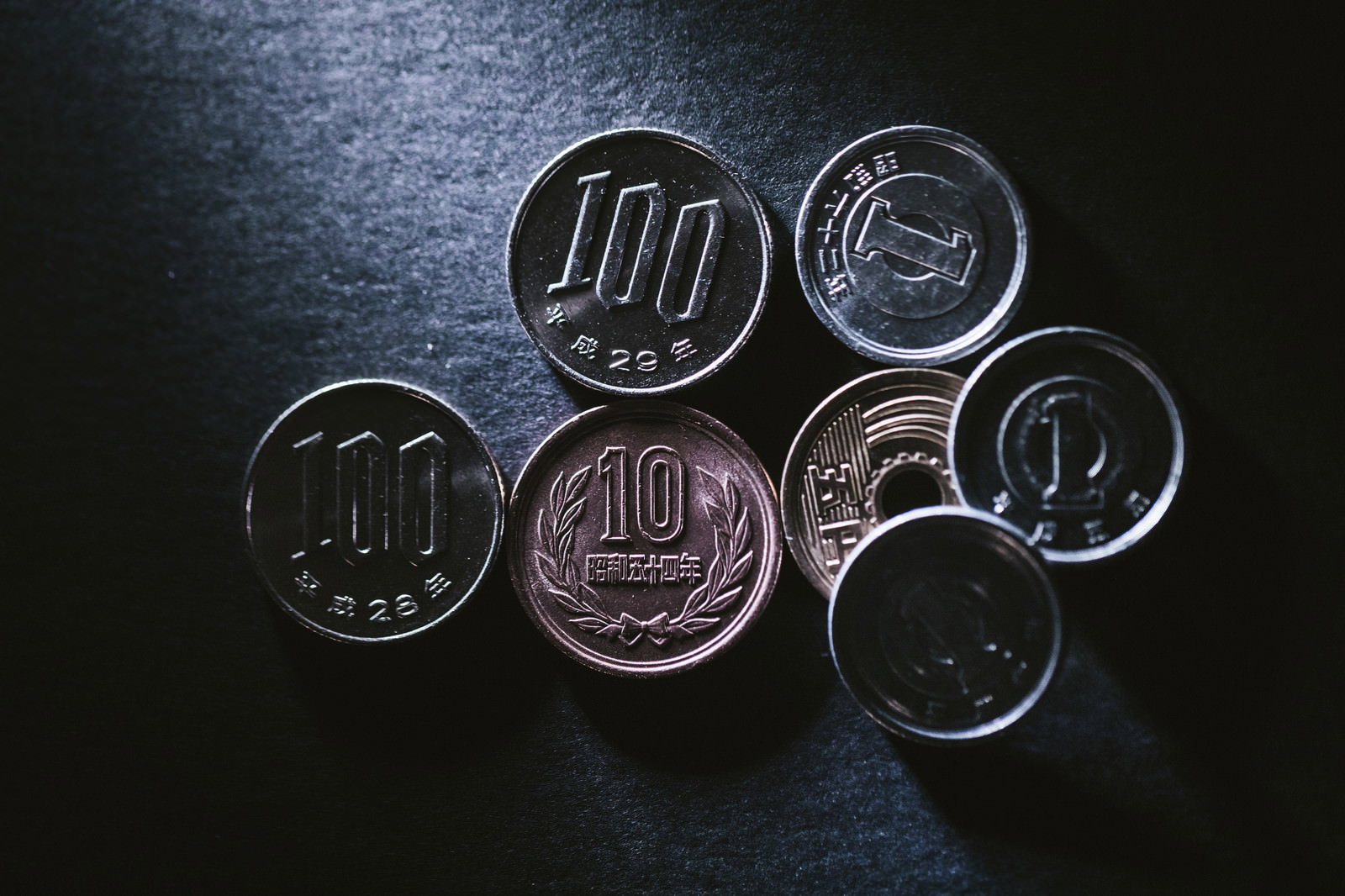暗いテーブルの上に整然と並べられた6枚の100円硬貨