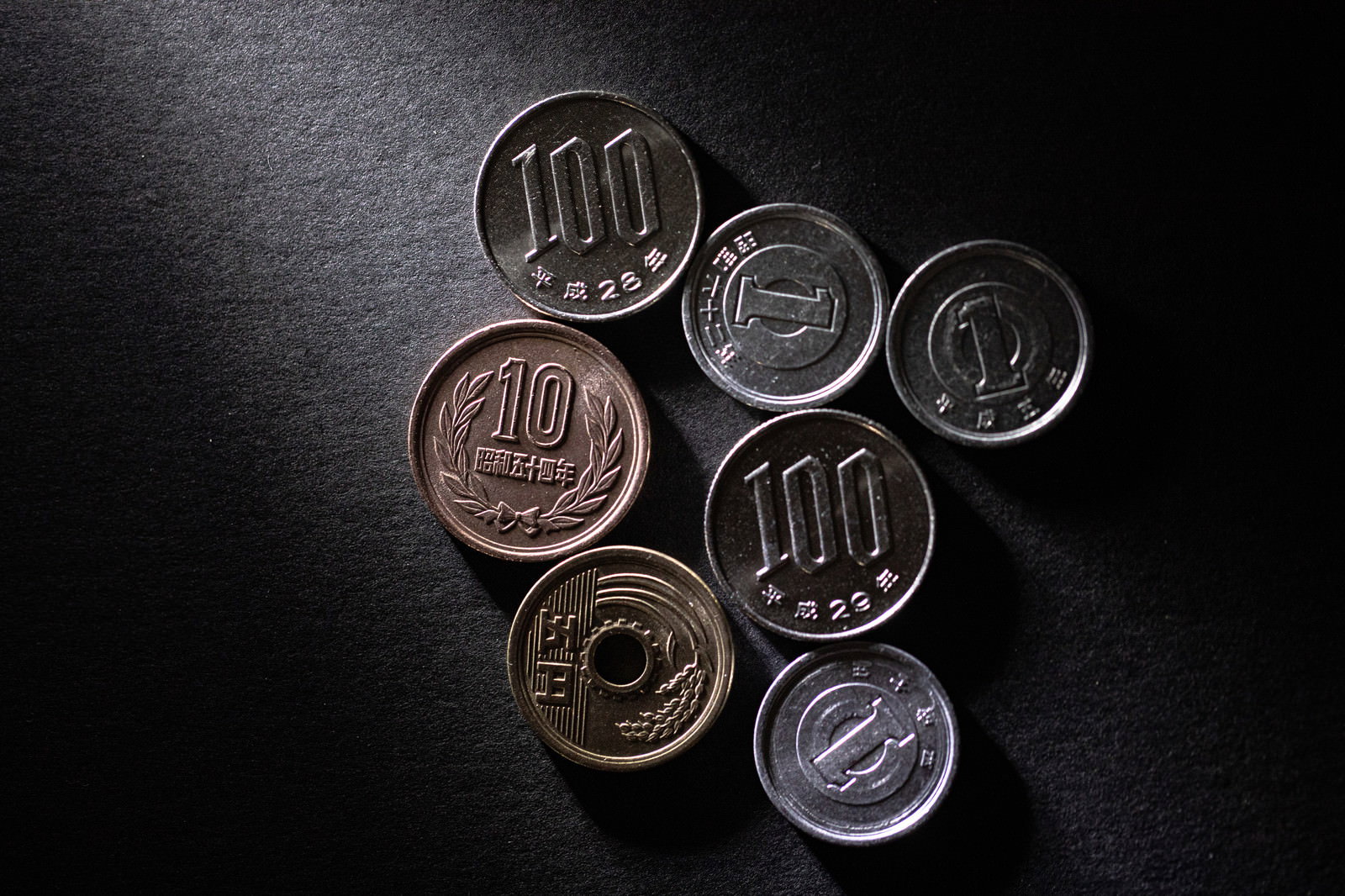 黒いテーブルの上に散らばって置かれた日本の硬貨数枚