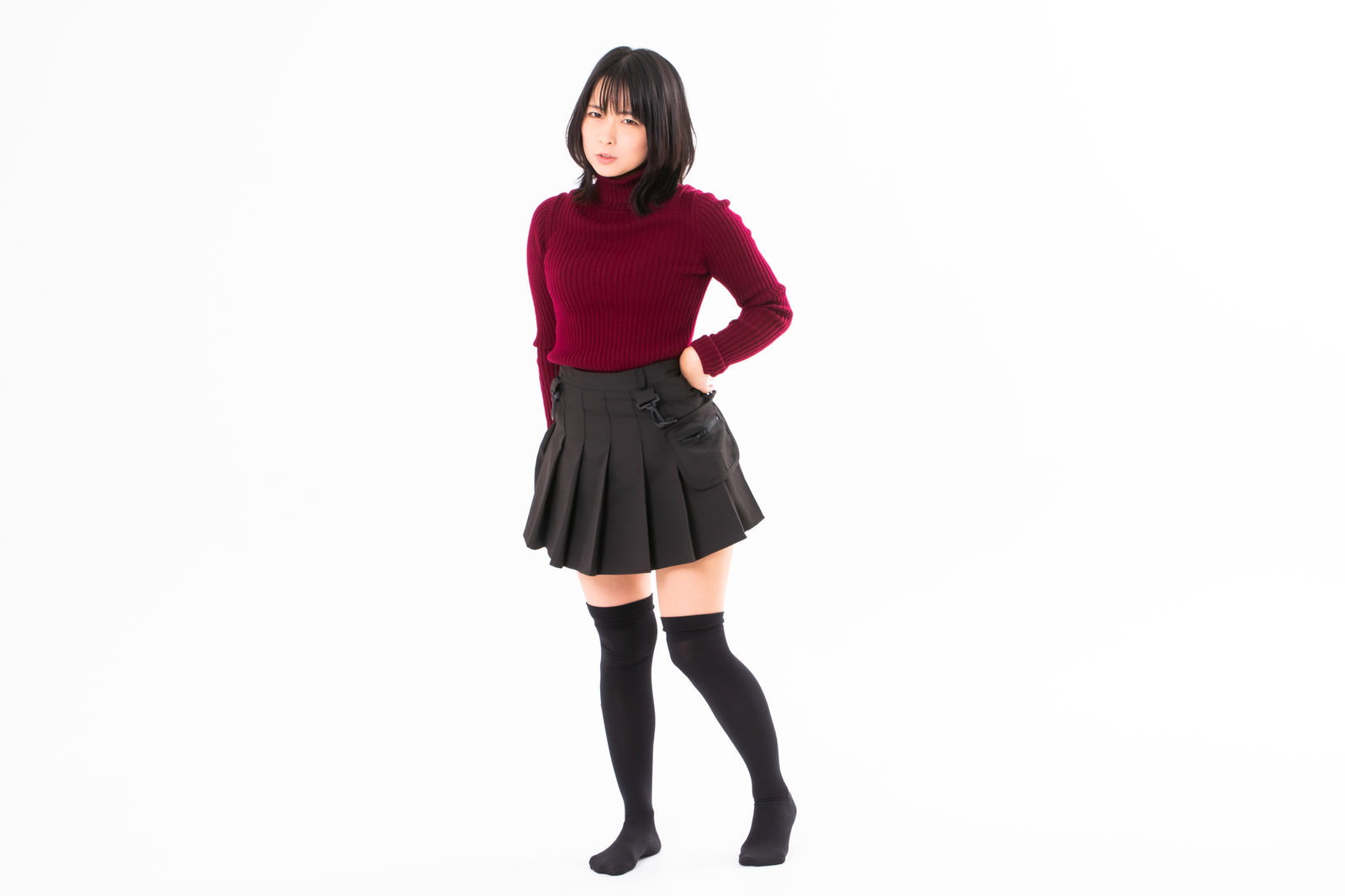 腰に手を当てて不機嫌な表情をする赤いニットの女性［モデル：にゃるる］