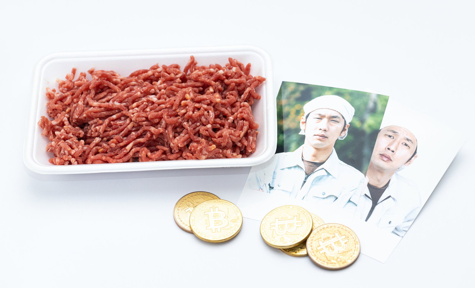 白い背景に置かれたパック入りミンチ肉と仮想通貨コイン［モデル：大川竜弥］