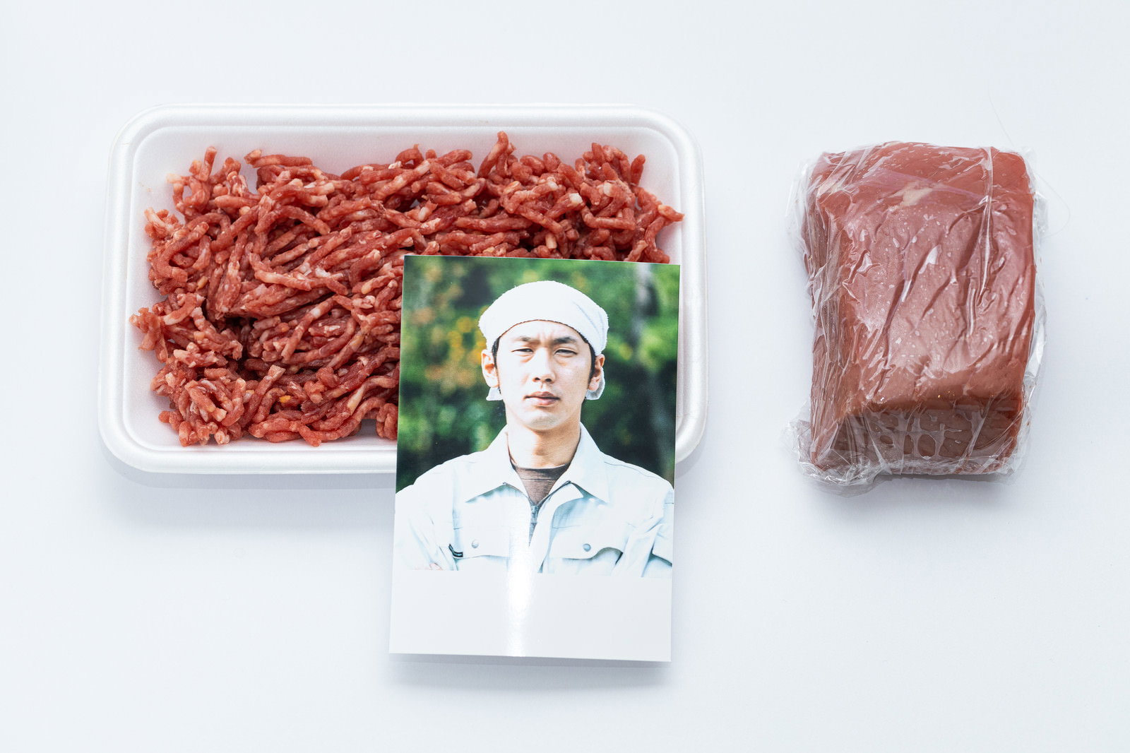 透明トレーに入った挽肉とパック入りブロック肉、生産者の顔写真［モデル：大川竜弥］