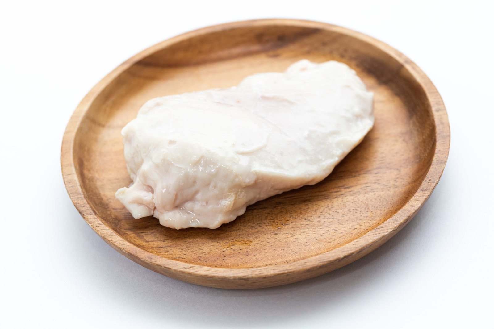 木製の丸い皿に盛り付けられた白いサラダチキンの鶏胸肉