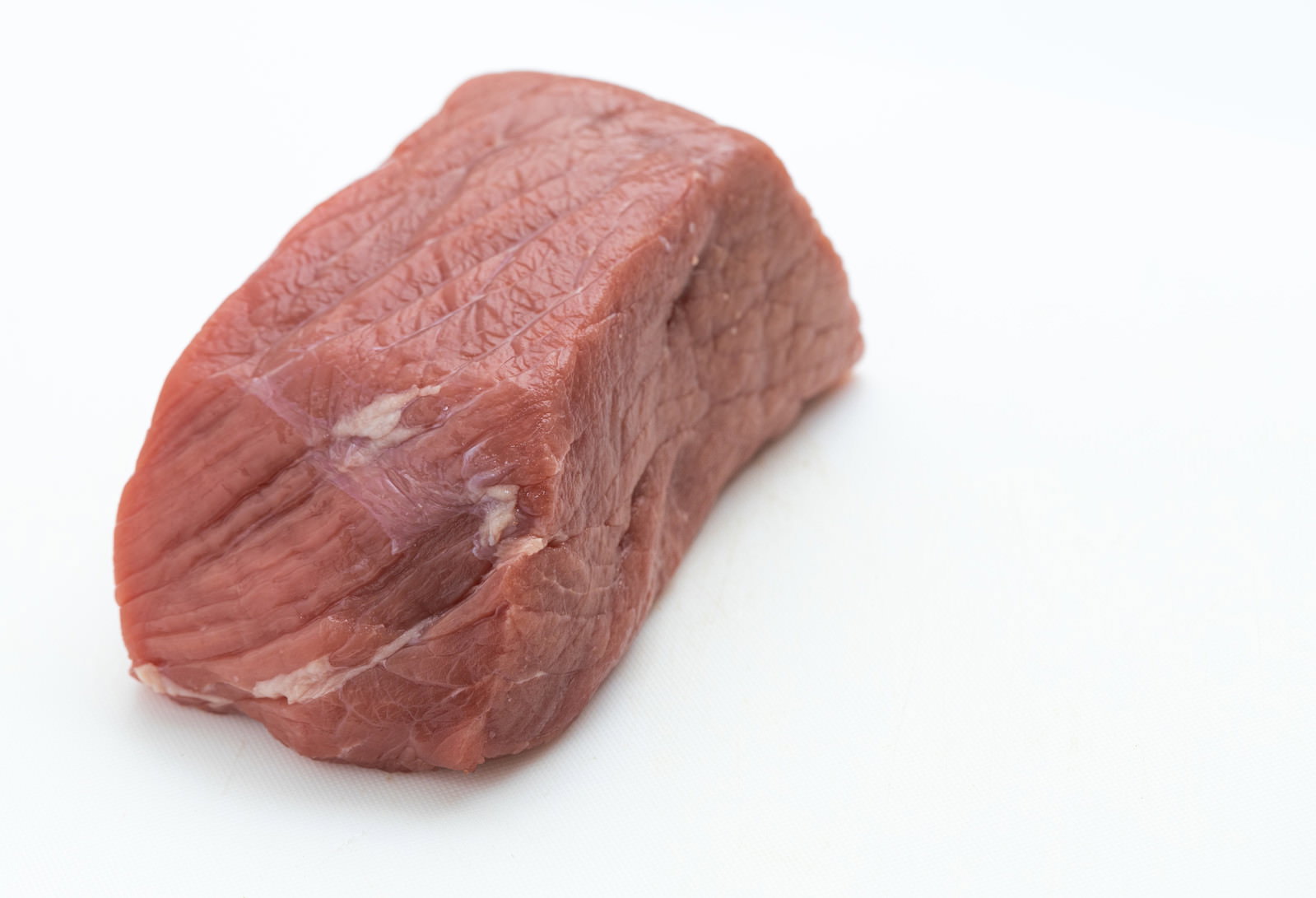 白い背景に置かれた赤身の牛のモモ肉のブロック