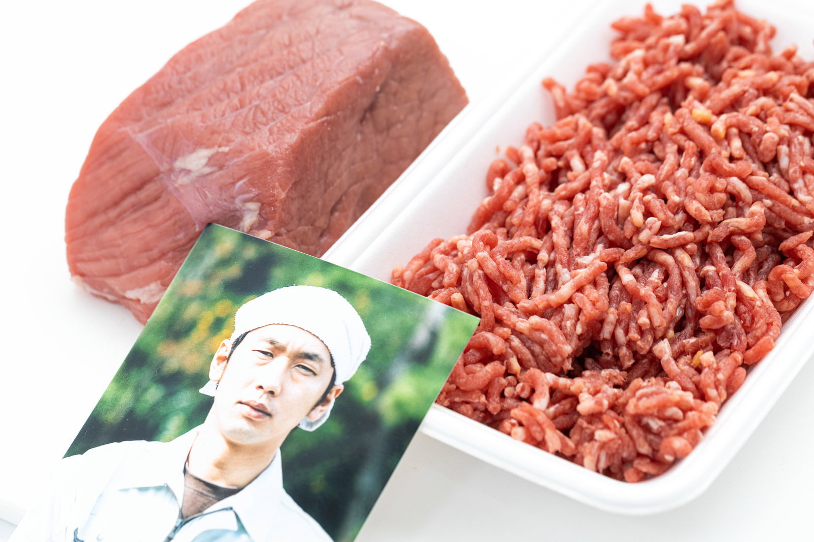 白いトレーに盛られたミンチ肉と生産者の顔写真［モデル：大川竜弥］