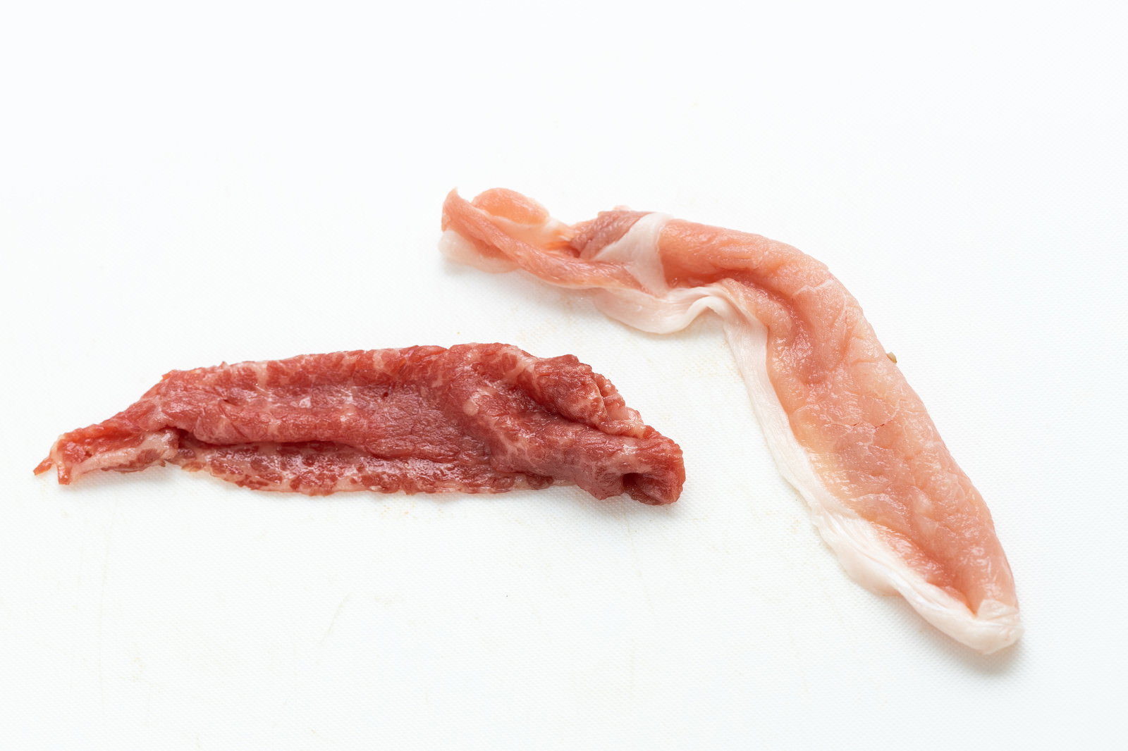 白い背景に置かれた豚肉ロースと牛肉モモ肉の生肉