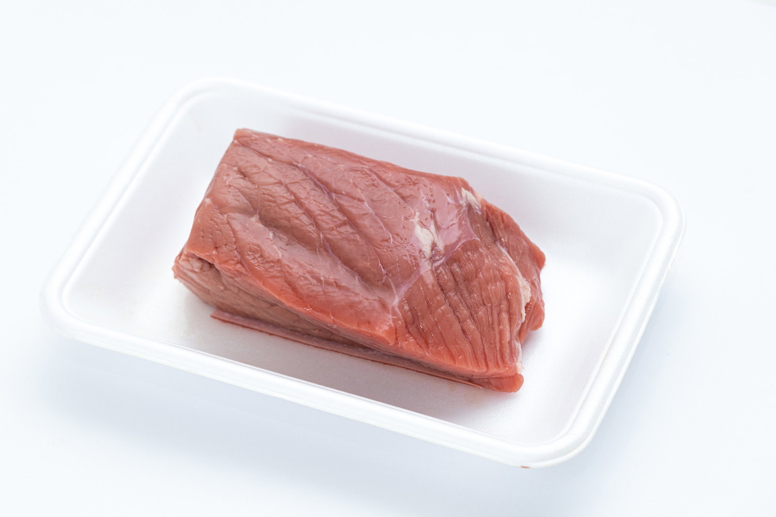 白い食品トレーに入った赤身の牛モモ肉のブロック