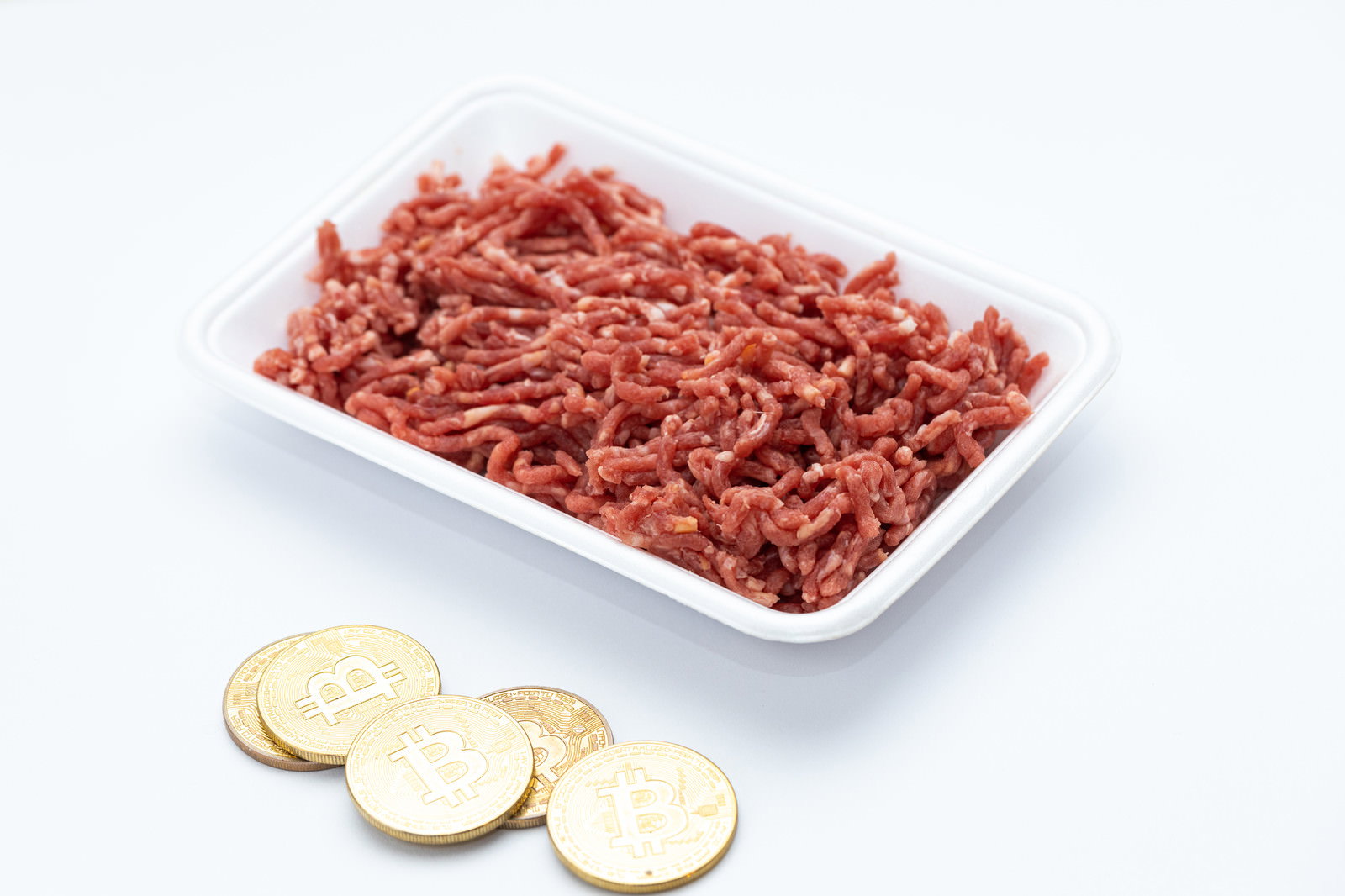 白いトレーに盛られた赤い挽肉と手前に置かれた3枚の金色のビットコイン