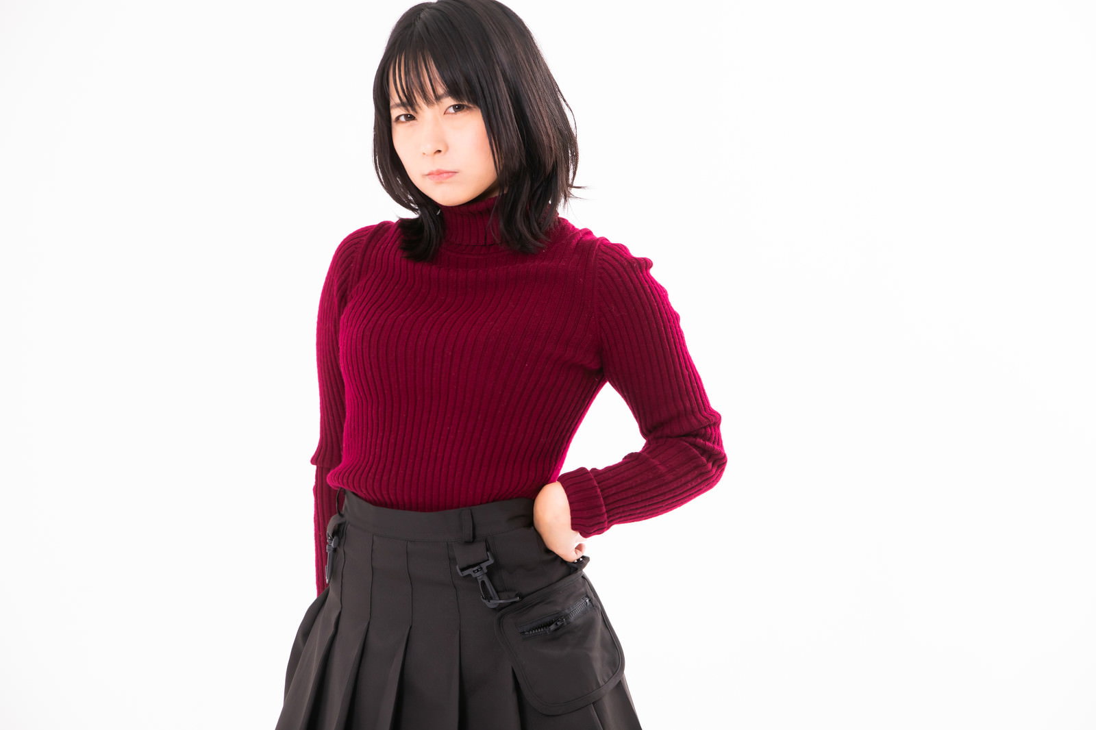 赤いタートルネックを着て腰に手を当て不機嫌な表情をする女性［モデル：にゃるる］