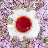 敷き詰められた紫のライラックに囲まれたティーカップの紅茶の写真