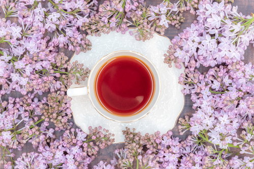 敷き詰められた紫のライラックに囲まれたティーカップの紅茶