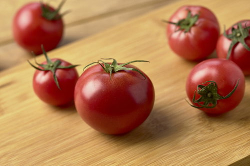木製まな板の上に置かれた蔕付きミニトマトの写真