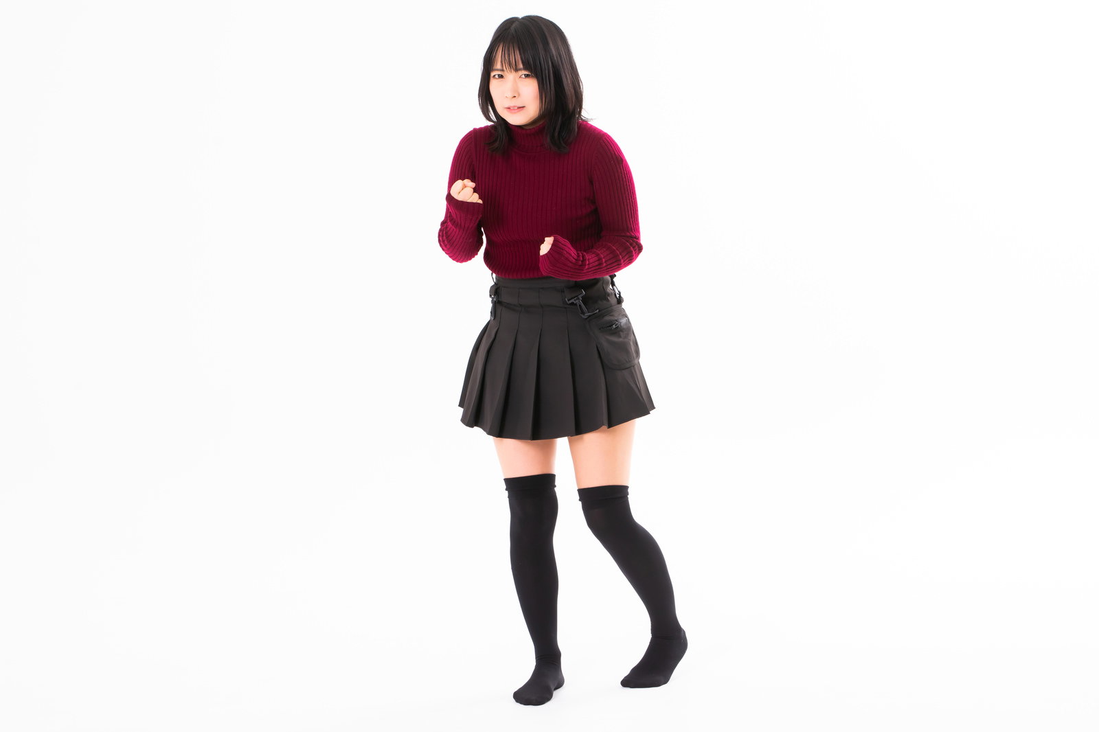 赤いトップスと黒いスカートの女性が両手を拳にして我慢している様子［モデル：にゃるる］