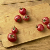 木製のまな板に並ぶ蔕付きミニトマト6個の新鮮な食材の写真