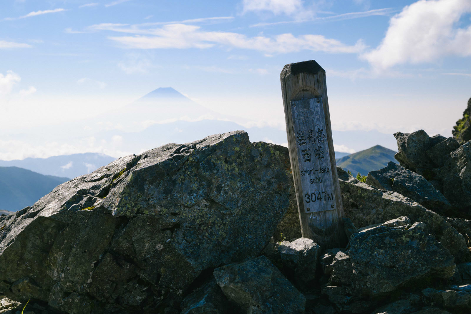 塩見岳西峰の山頂標識と遠くに霞む南アルプスの山々