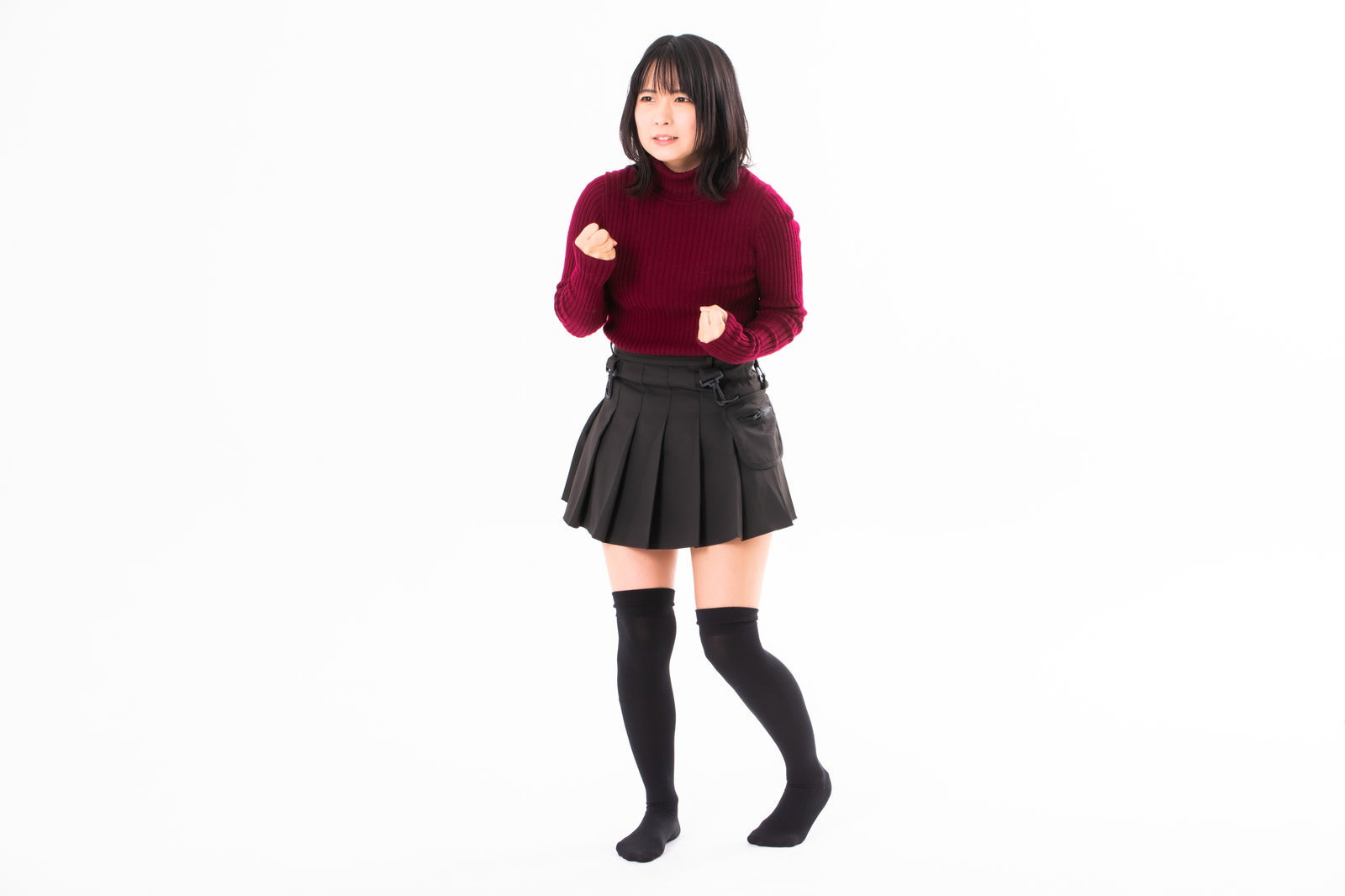 赤いニットを着た女性が両手で拳を握りしめてイライラしている［モデル：にゃるる］